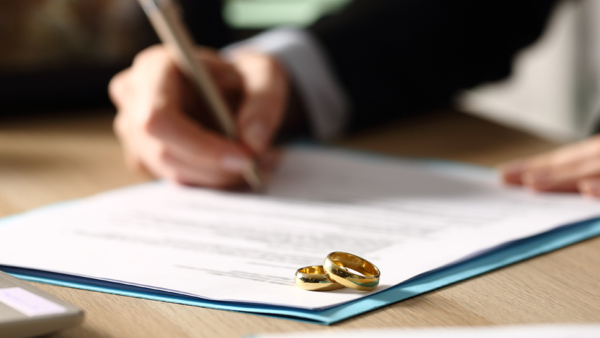 Hand signing documents with wedding rings next to them